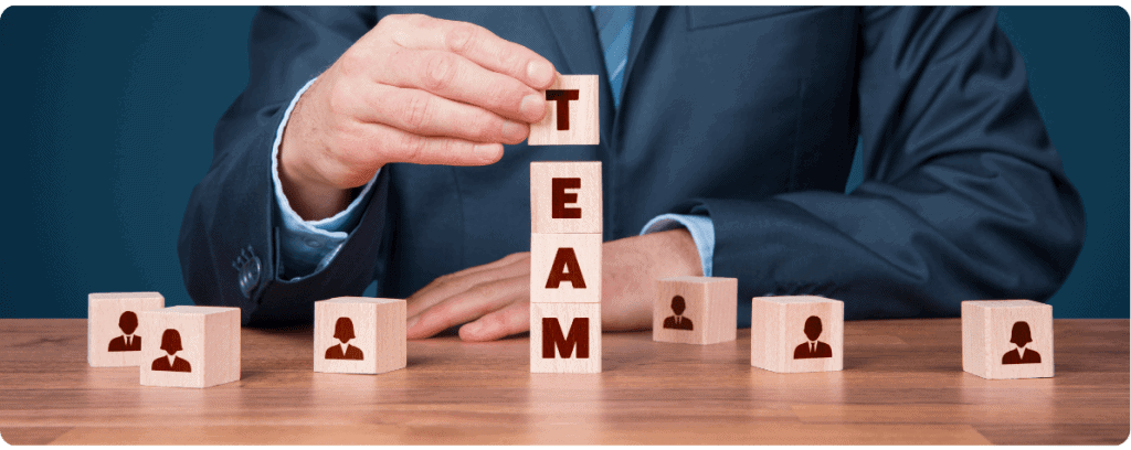 5 důvodů, proč je outsourcing IT specialistů výhodnou strategií 6 Člověk v obleku skládá kostky s ikonami lidí a nápisem TEAM, symbolizující týmovou práci.