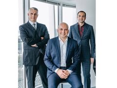 Tři muži v oblecích na poradě v moderní kanceláři.