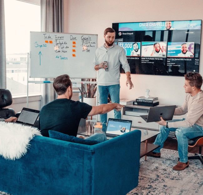 Skupina lidí při poradě s notebooky a velkou obrazovkou v zasedací místnosti.