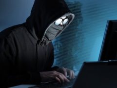 Osoba v kapuci pracující na počítači, kybernetický útok, bezpečnostní hrozba.